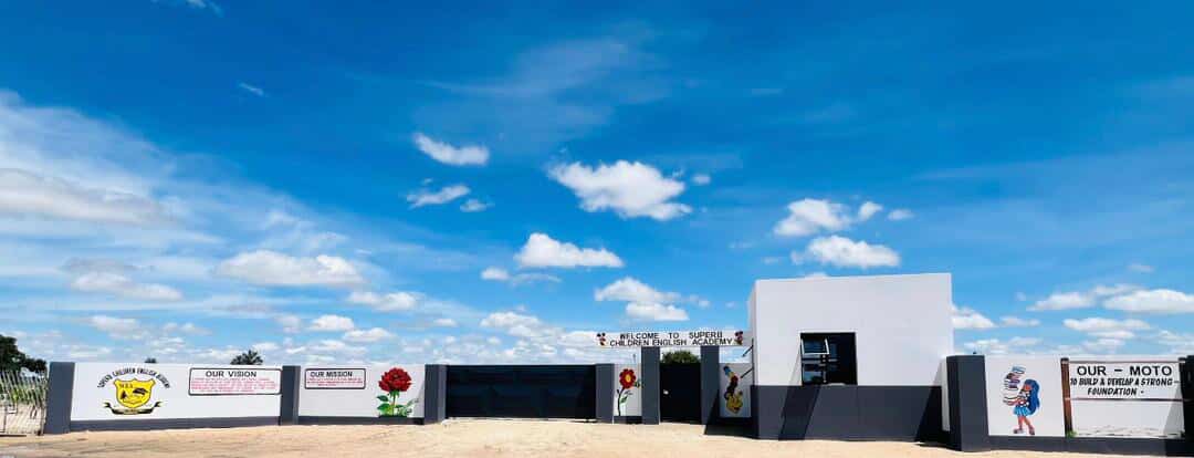 Entrance wall of Superb Children English Academy with vision, mission and motto boards under a blue sky