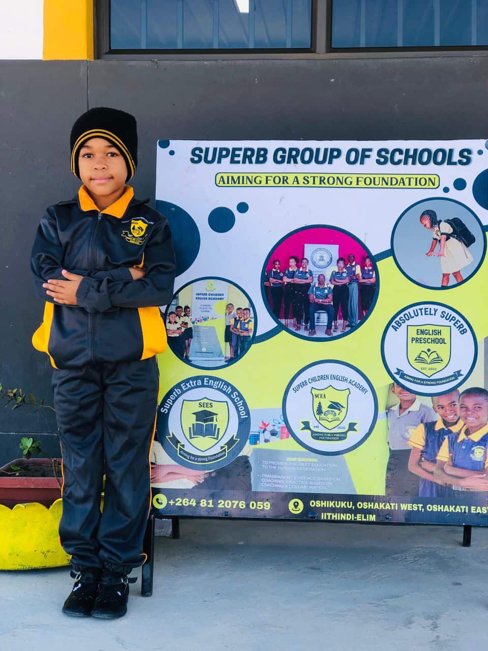 Learner in a winter tracksuit standing beside the Superb Group of Schools banner