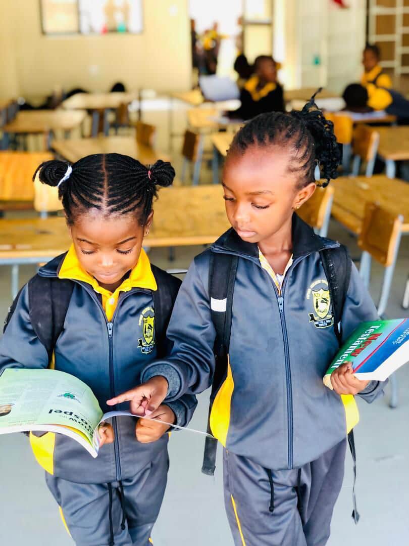 Two learners in tracksuits reading a booklet together in the school hall