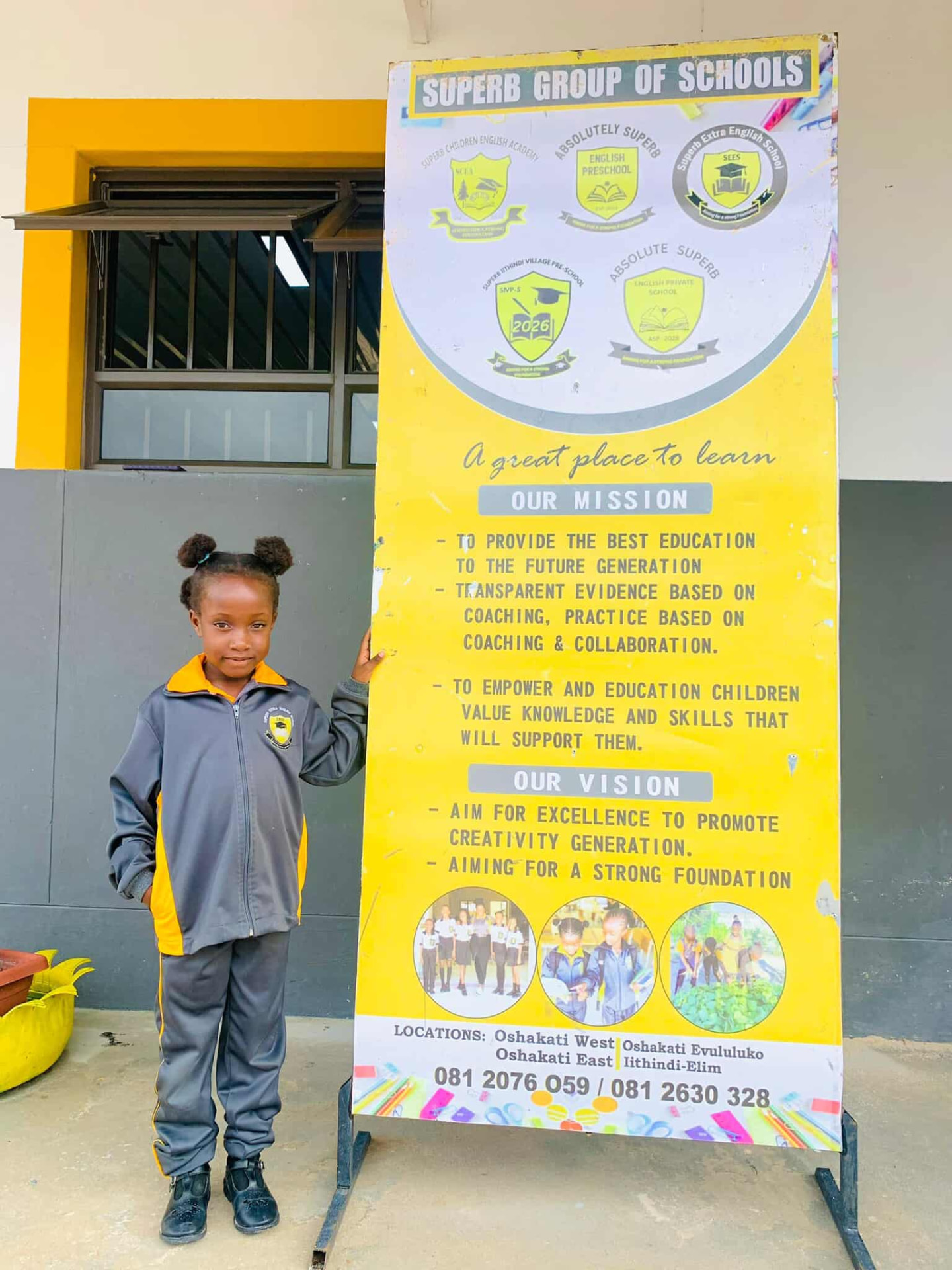 Young learner standing beside the Superb Group of Schools mission and vision banner