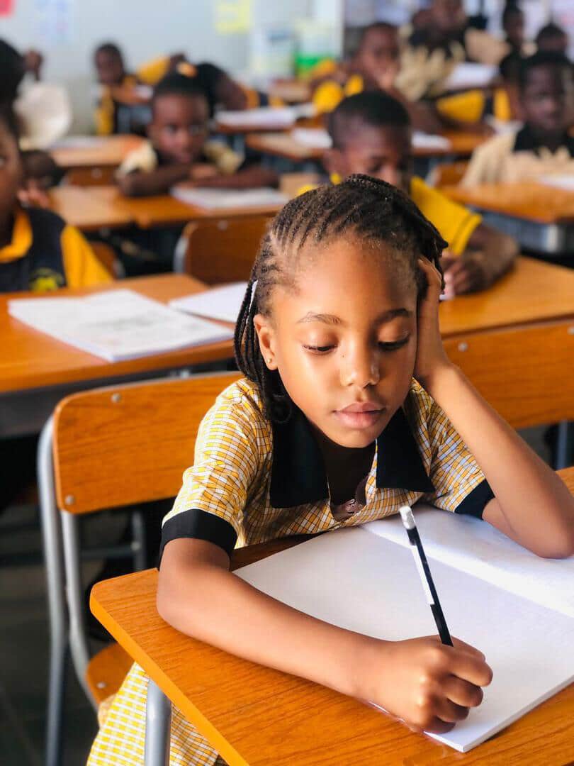 Learner in a yellow checked uniform writing in her exercise book at her desk