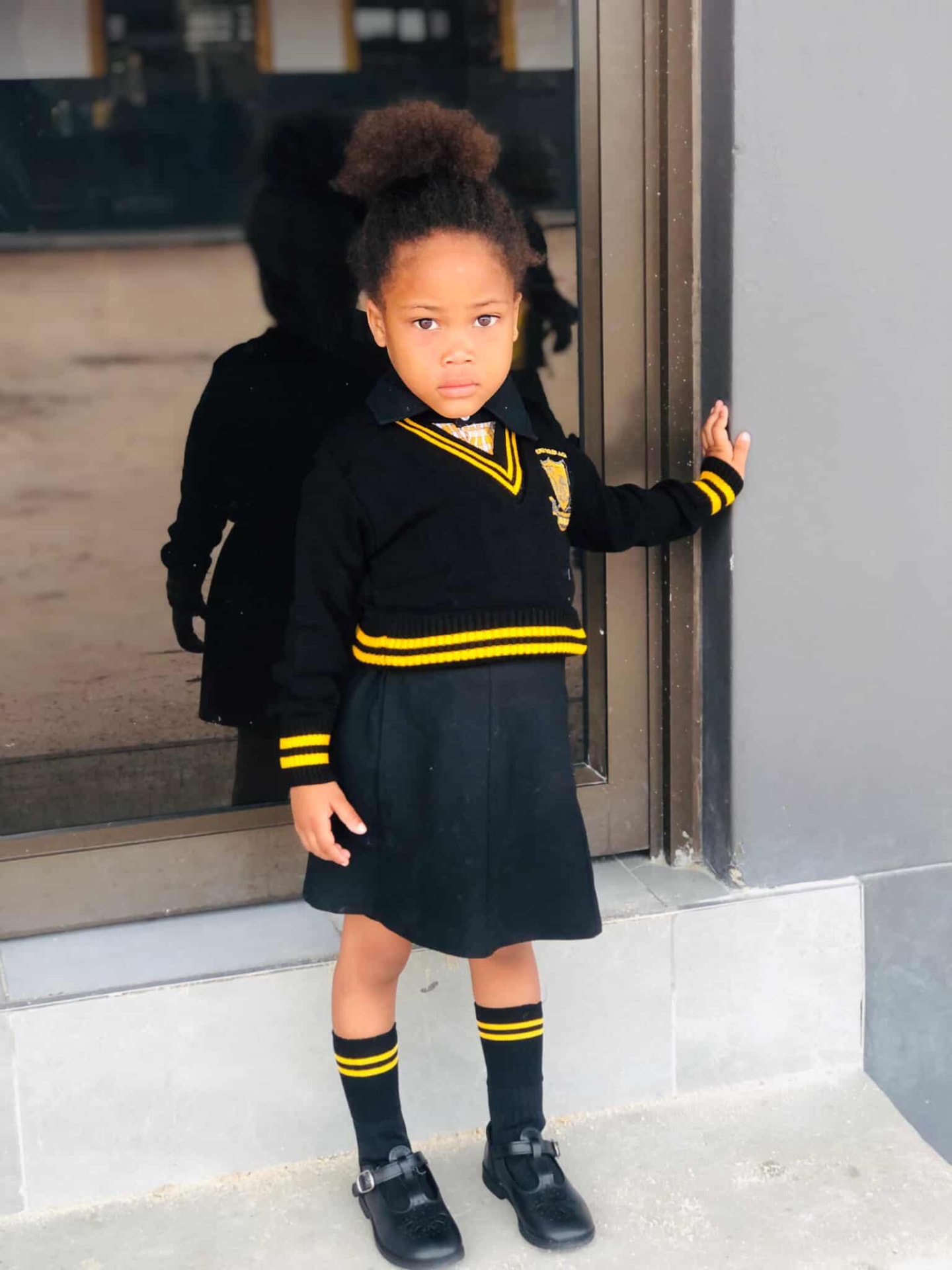 Young learner in a black and gold school jersey and skirt standing by a classroom door