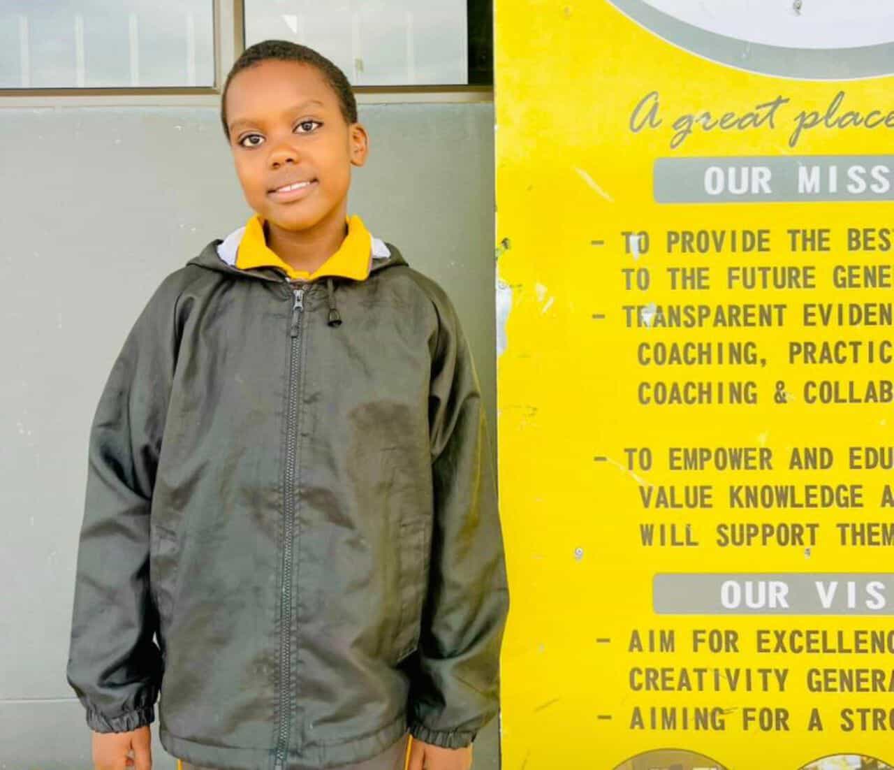 Senior primary learner standing beside the school mission and vision board