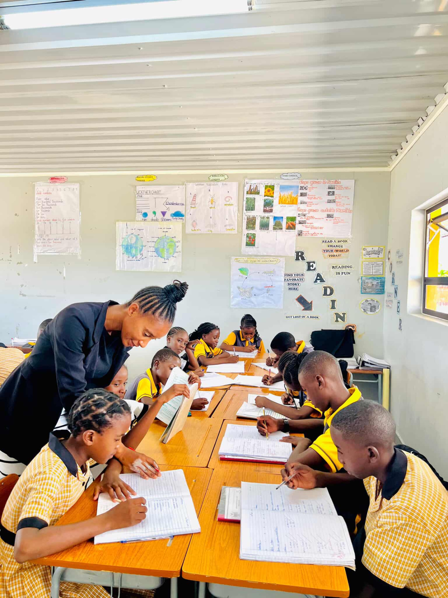 Teacher guiding learners writing in their books at long shared desks