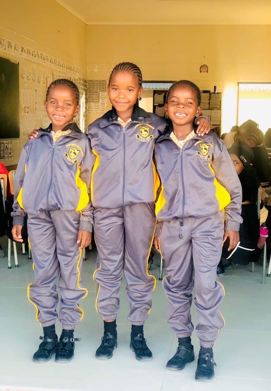 Three learners in tracksuits standing arm in arm in their classroom