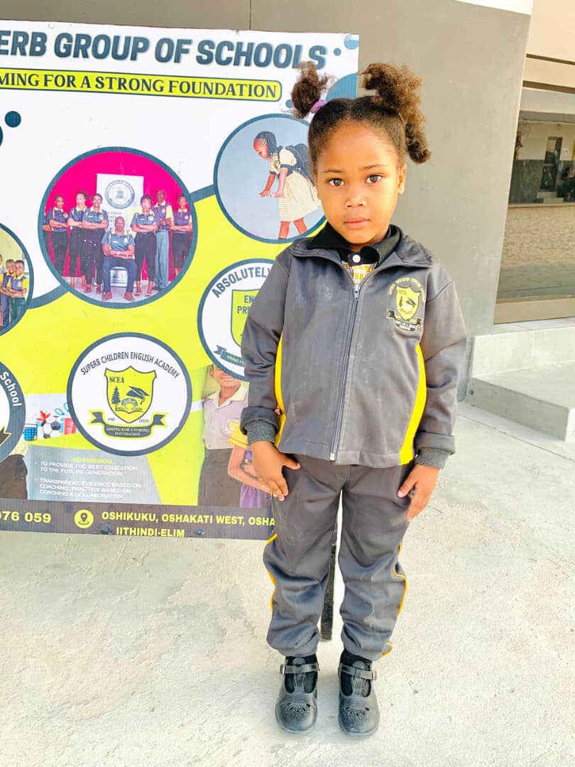 Preschool learner in a tracksuit standing in front of the Superb Group of Schools banner