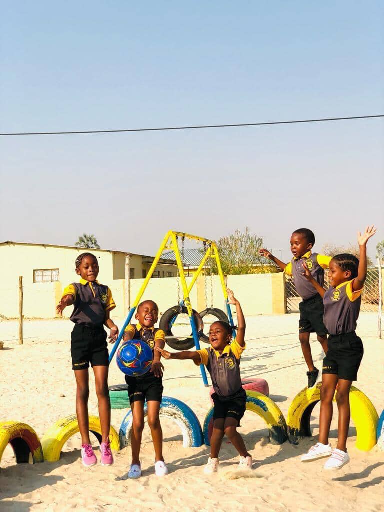 Five preschool learners playing with a ball on the swings and painted tyres