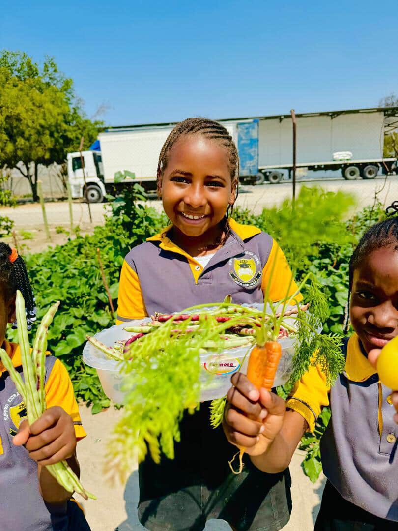 Learners holding a tray of beans and freshly pulled carrots in the school garden