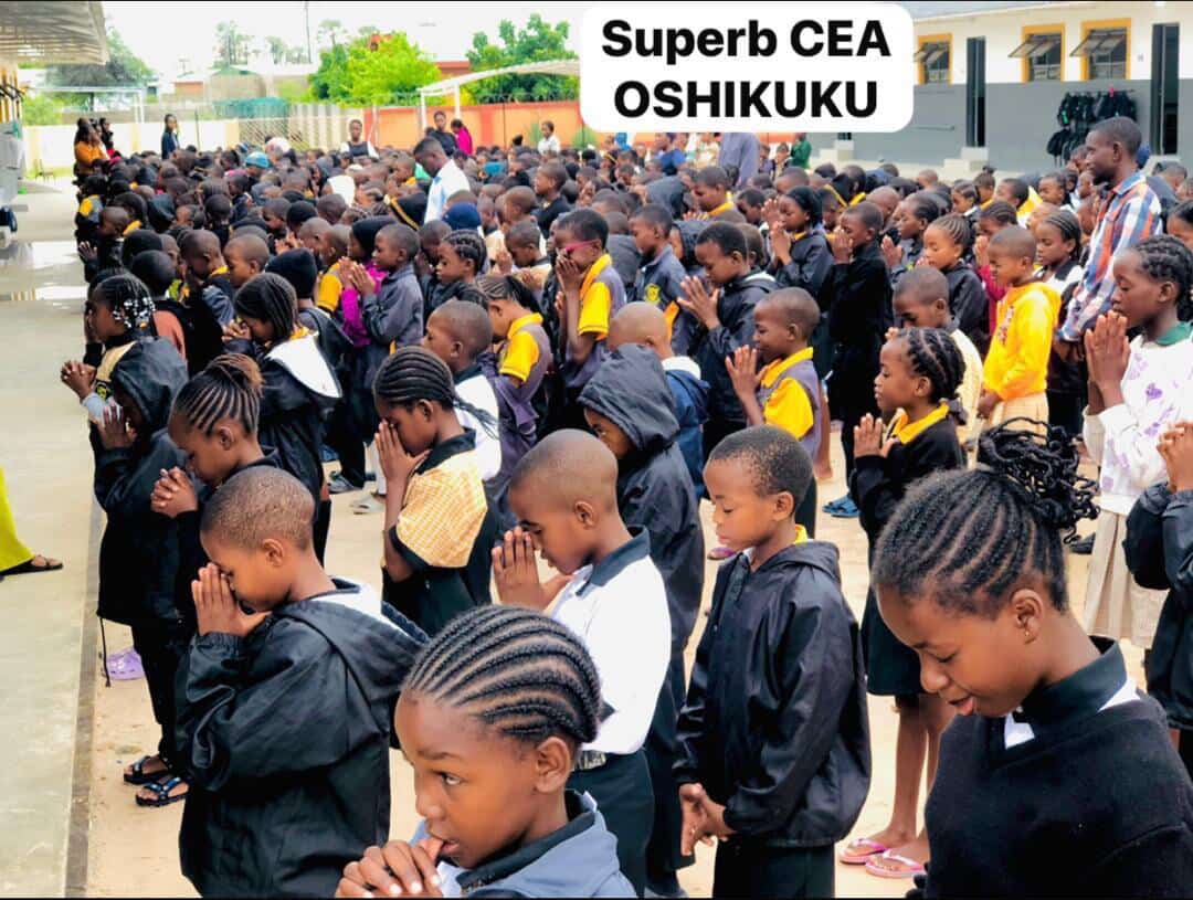 Learners standing in rows with hands together during morning prayer at Superb CEA Oshikuku