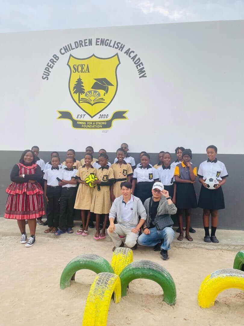 Learners and staff posing with visitors in front of the Superb Children English Academy crest wall