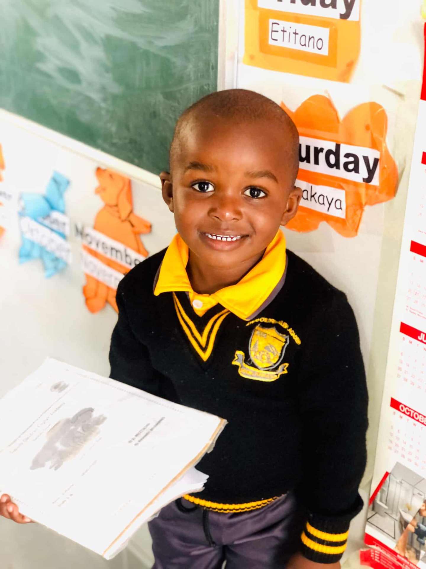 Young preschool learner smiling while holding his workbook in class