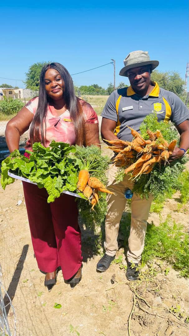 Two staff members holding freshly harvested carrots and spinach from the school garden