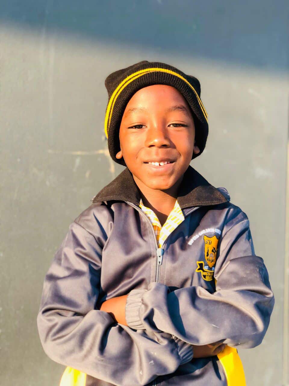Learner in a school beanie and tracksuit jacket standing with arms folded